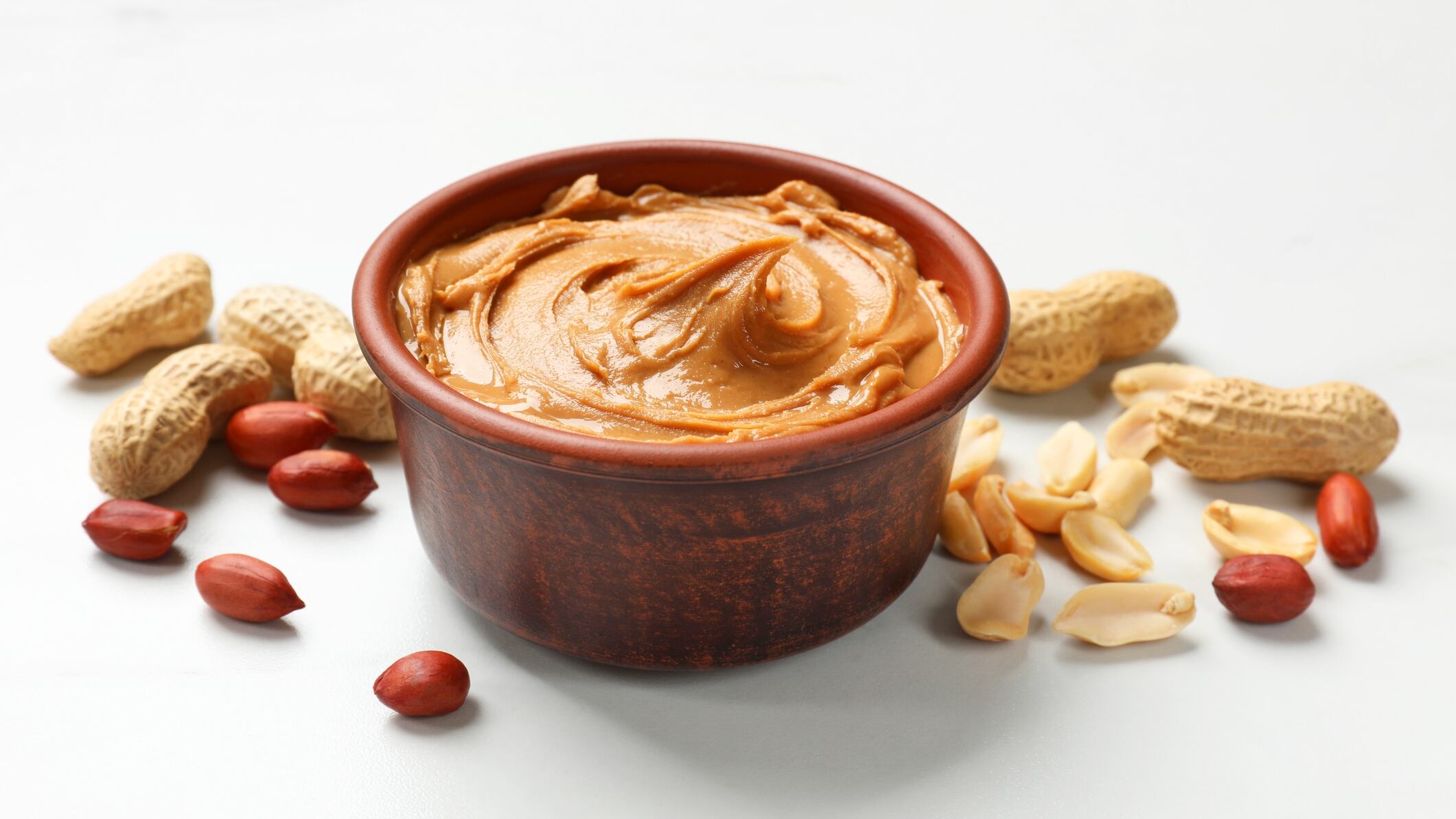 Tasty peanut butter in bowl and groundnuts on white table